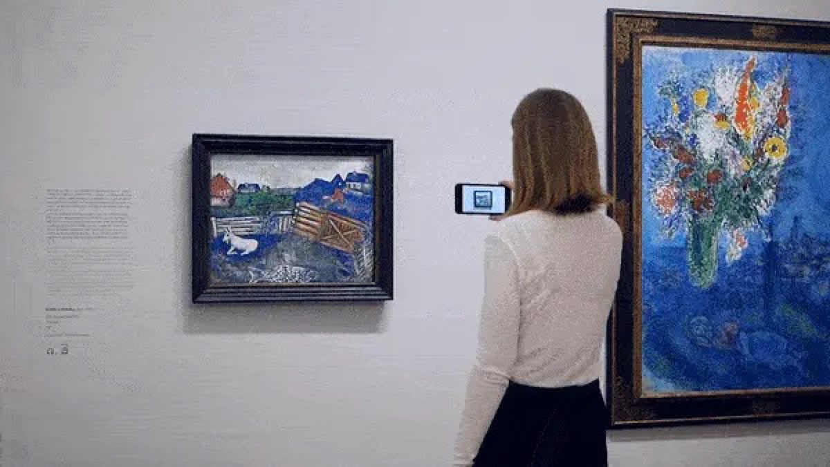 A visitor pointing a phone at a painting to see it augmented in a gallery